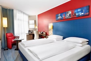 Une chambre d’hôtel avec un lit, un bureau, une chaise, une lampe et un tableau au mur.