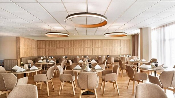 Ein geräumiger Konferenzraum mit runden Tischen, moderner Beleuchtung und einer Wand aus Holzpaneelen.