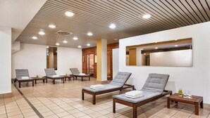 Ein Wellnessraum mit mehreren Liegestühlen, einer Holzbalkendecke und einem gefliesten Boden.