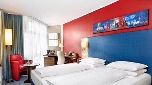 Ein Hotelzimmer mit einem Bett, einem Schreibtisch, einem Stuhl, einer Lampe und einem Bild an der Wand.