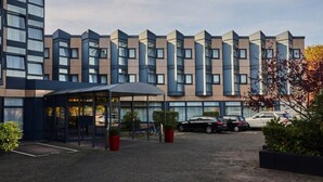 Ein modernes Hotel mit einer Reihe rechteckiger Fenster, einem überdachten Eingangsbereich und einem Parkplatz.