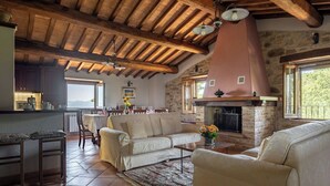 A spacious living area with a high wooden ceiling, a stone fireplace, and a kitchen in the background. - Villa Daluma, Private Pool in Todi (Todi)