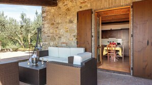 An outdoor seating area with wicker furniture, a stone wall, and a view of the kitchen. - Villa Daluma, Private Pool in Todi (Todi)