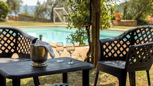 A poolside table with a metal container and two glasses, surrounded by chairs with a lattice backrest, with a pool and greenery in the background. - Villa Daluma, Private Pool in Todi (Todi)