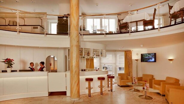 Et hotel lobby med receptionsdisk, barstole, siddeområde og et fjernsyn.