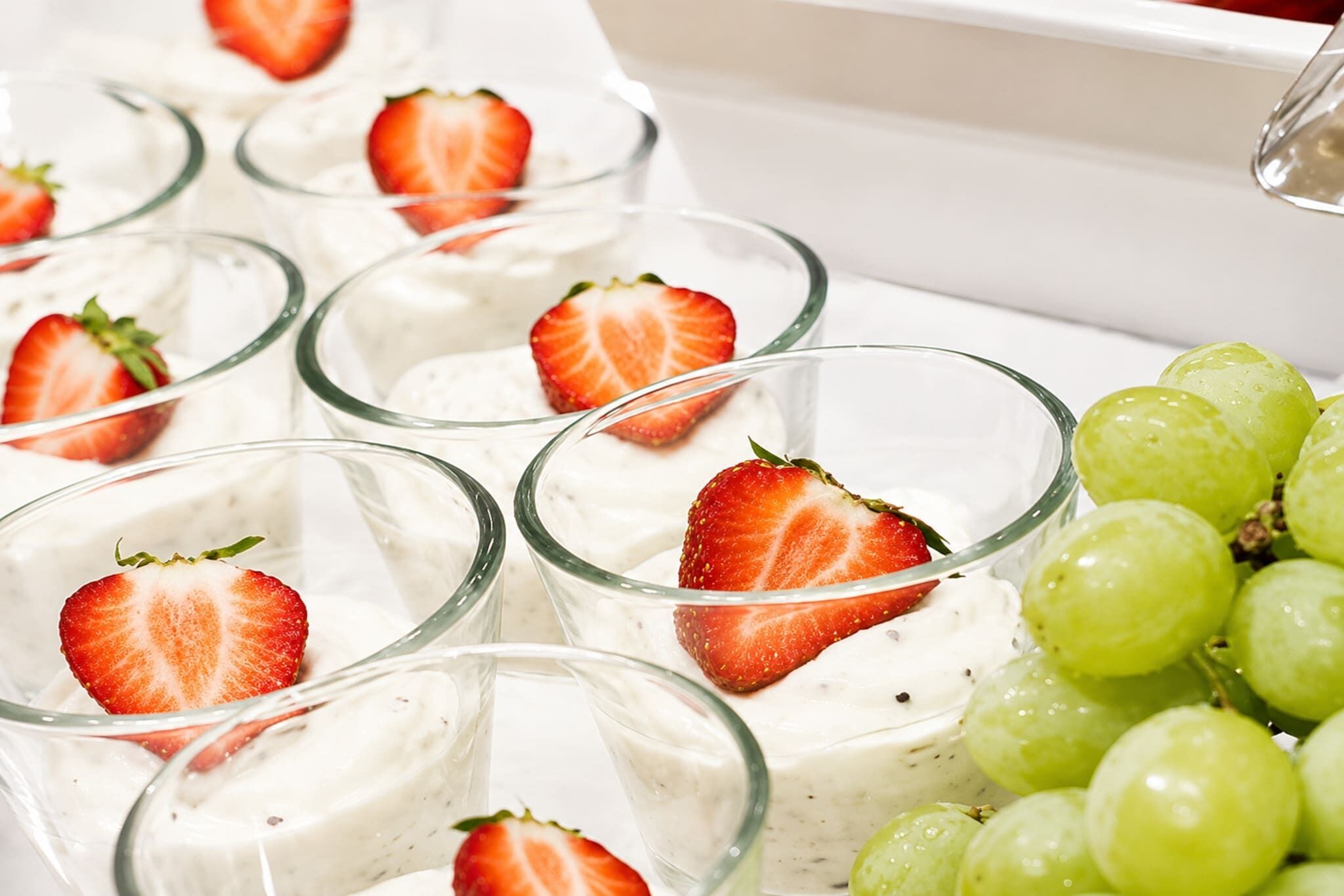 A dessert tray with individual servings of a white creamy dessert topped with strawberries and garnished with grapes.