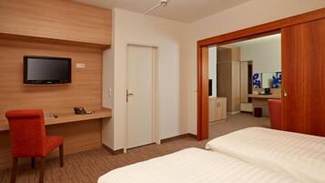 Habitación de hotel con cama, escritorio con silla, televisor montado en la pared y puerta que da a otra habitación.