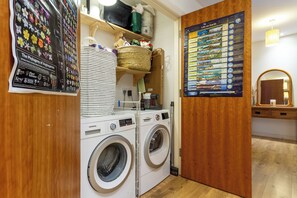 A laundry area with two front-loading washing machines, a drying rack, and a poster on the wall. - Leafy Leith 2BDR Retreat with a Private Balcony (Edinburgh)