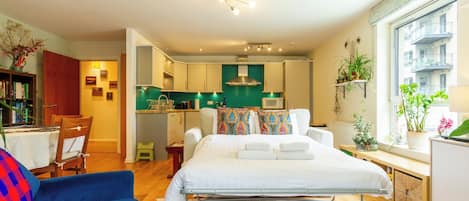 A compact hotel room with a bed, a small kitchenette, a dining area, and a view of the city.
