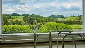 Una habitación con un ventanal grande que da a un paisaje verde con árboles y colinas.