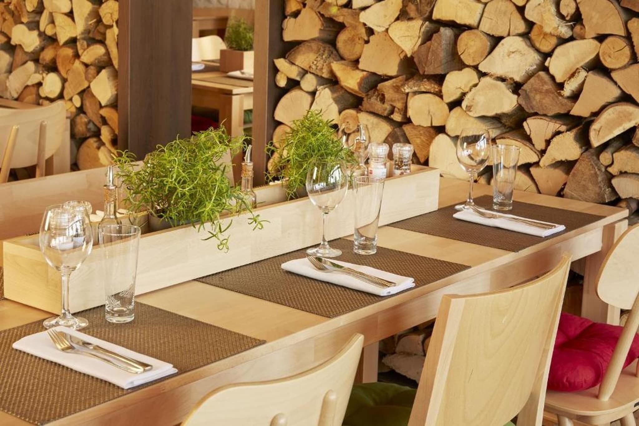 Une table à manger dressée avec de la verrerie, un arrangement floral en guise de centre de table et, en arrière-plan, une pile de bois de chauffage.