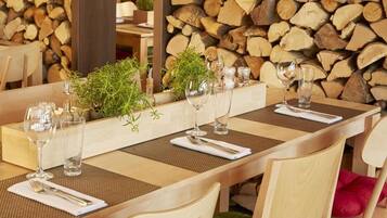 Une table à manger dressée avec de la verrerie, un arrangement floral en guise de centre de table et, en arrière-plan, une pile de bois de chauffage.