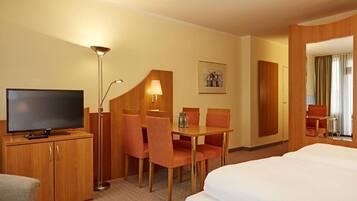 Habitación de hotel con cama, televisión, escritorio y sillas, lámpara y un cuadro en la pared.