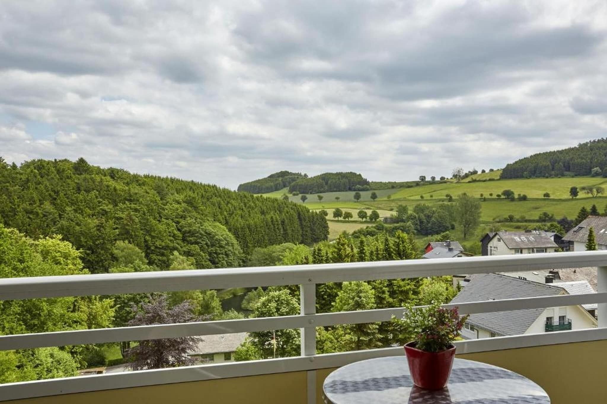 Un balcón con vistas a un paisaje verde, una pequeña mesa y una planta en maceta.