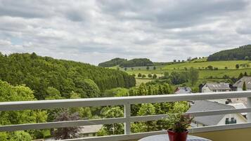 Un balcón con vistas a un paisaje verde, una pequeña mesa y una planta en maceta.