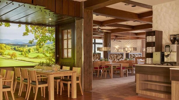 Un restaurante con mobiliario de madera, vistas a un campo de golf y una zona de cocina con máquinas de café.