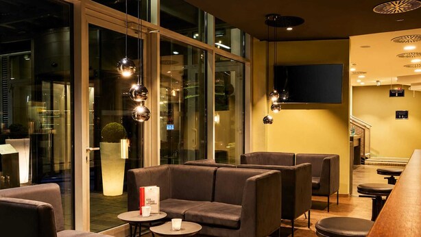 Un espacio lounge moderno con asientos de cuero, puertas de cristal e iluminación colgante.
