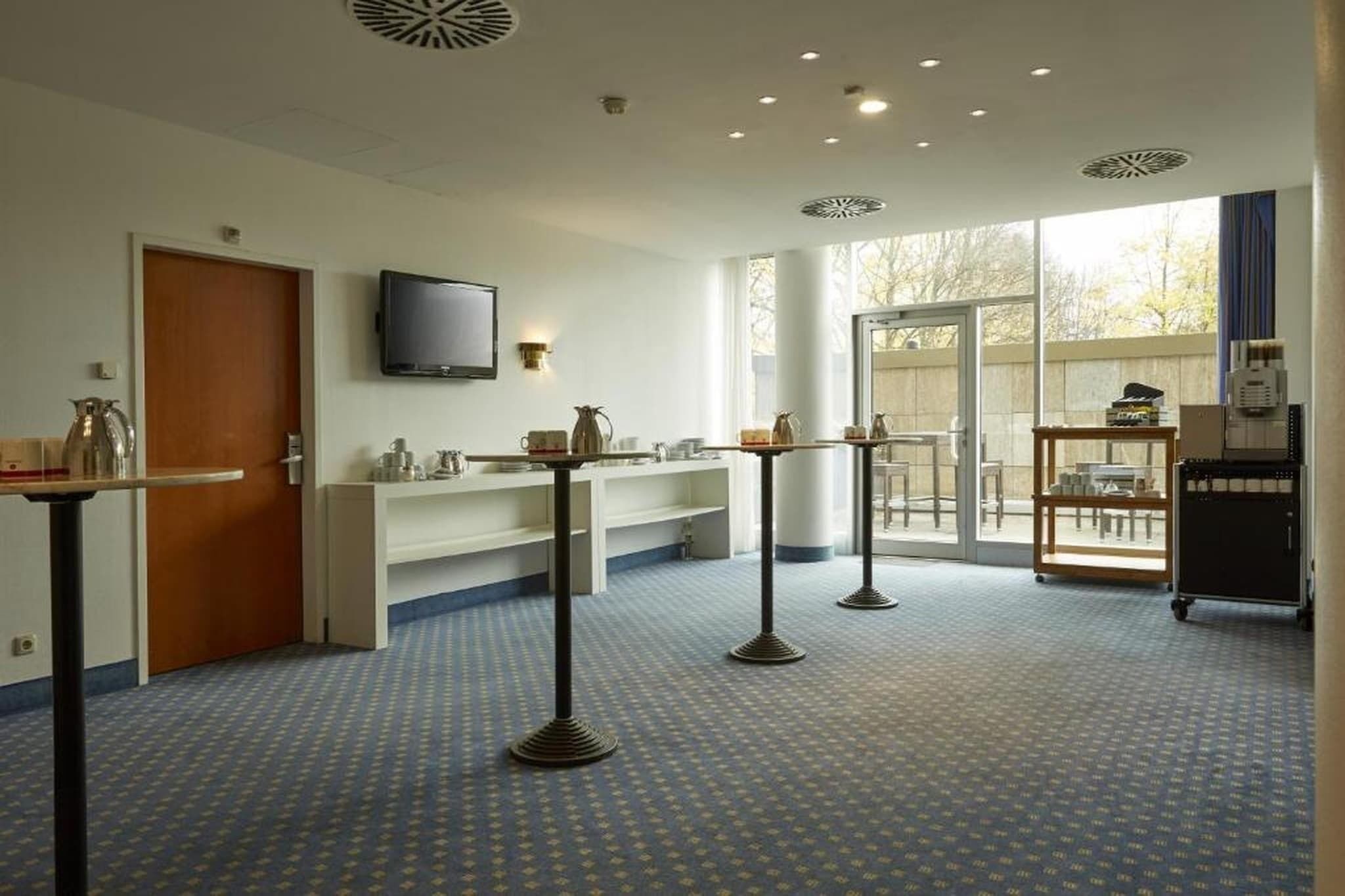 Ein Hotelzimmer mit großem Fenster, einem wandmontierten Flachbildfernseher, einer Küchenzeile und einer Sitzecke mit Tisch und Stühlen.