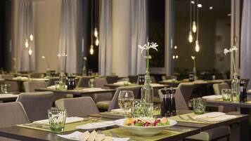 Ein Restaurant mit gedeckten Tischen, an jedem Tisch eine Wasserflasche, ein Glas und ein Teller mit Essen.