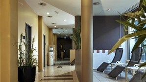 Een hotel lobby met een zwart-wit schachbordvloer, kamerplanten, een receptiebalie en ligbedden.