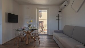 Una zona de menjador amb taula i cadires de vidre, un sofà, una televisió i un aparell d'aire condicionat.