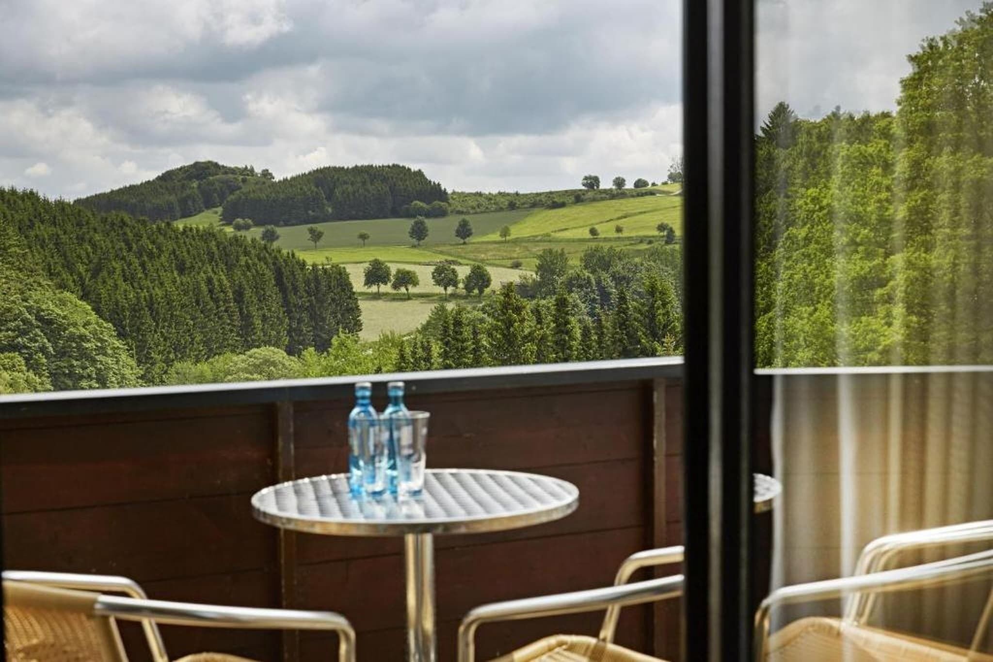 Un balcón con mesa y sillas, con vistas a un paisaje verde con colinas y árboles.