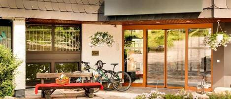 A building entrance with a bench, bicycles, and a hanging flower basket.