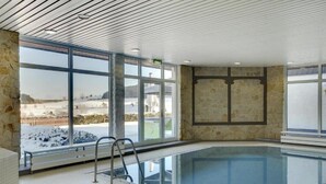 An indoor swimming pool with stone walls, large windows, and a view of a snowy landscape.