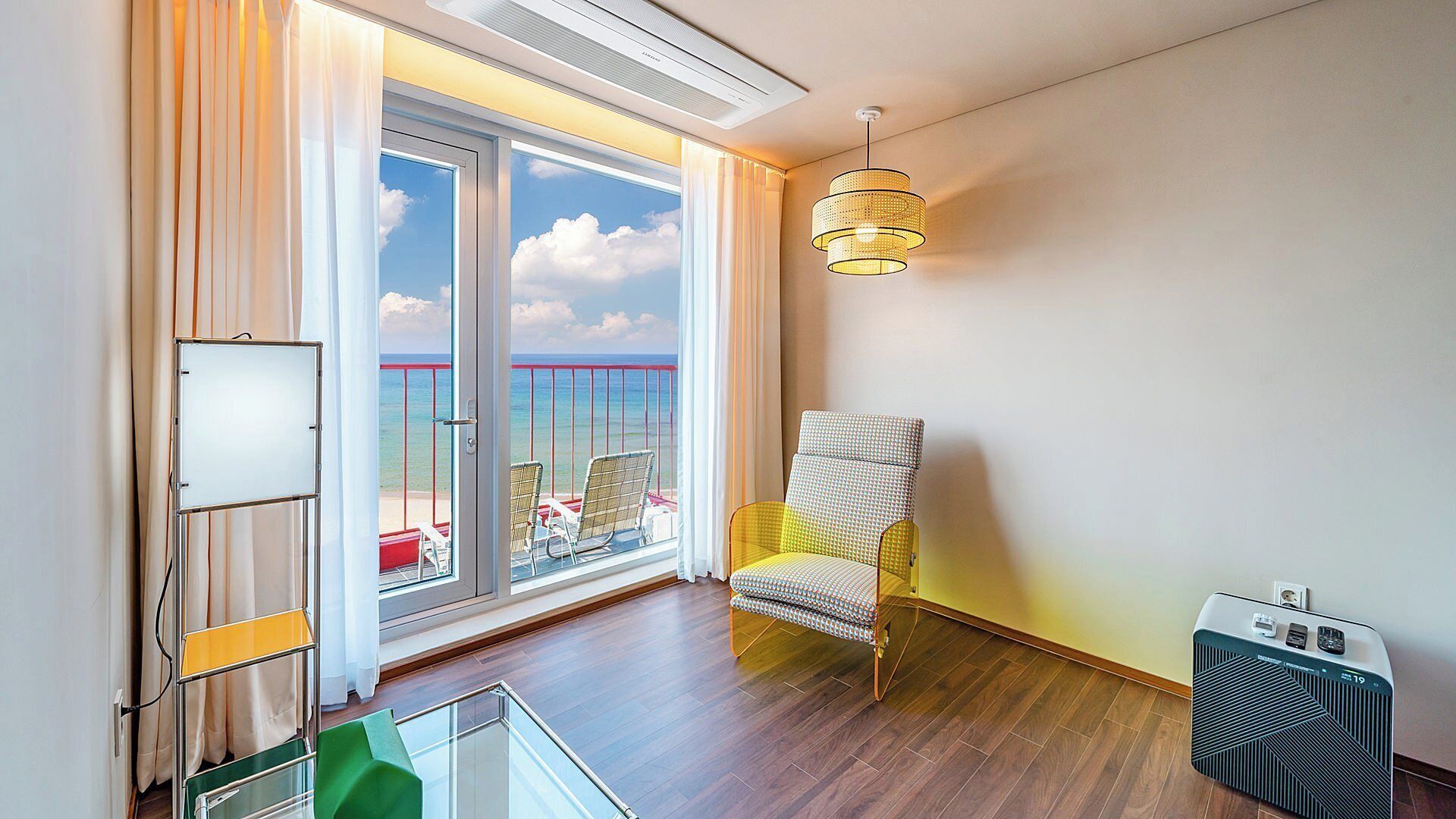 A room with a large sliding glass door to a balcony, a chair, a table, and a standing heater.