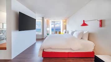 Een moderne hotelkamer met een groot bed, een rode accentmuur, een aan de muur bevestigde televisie en een balkon met uitzicht op de zee.
