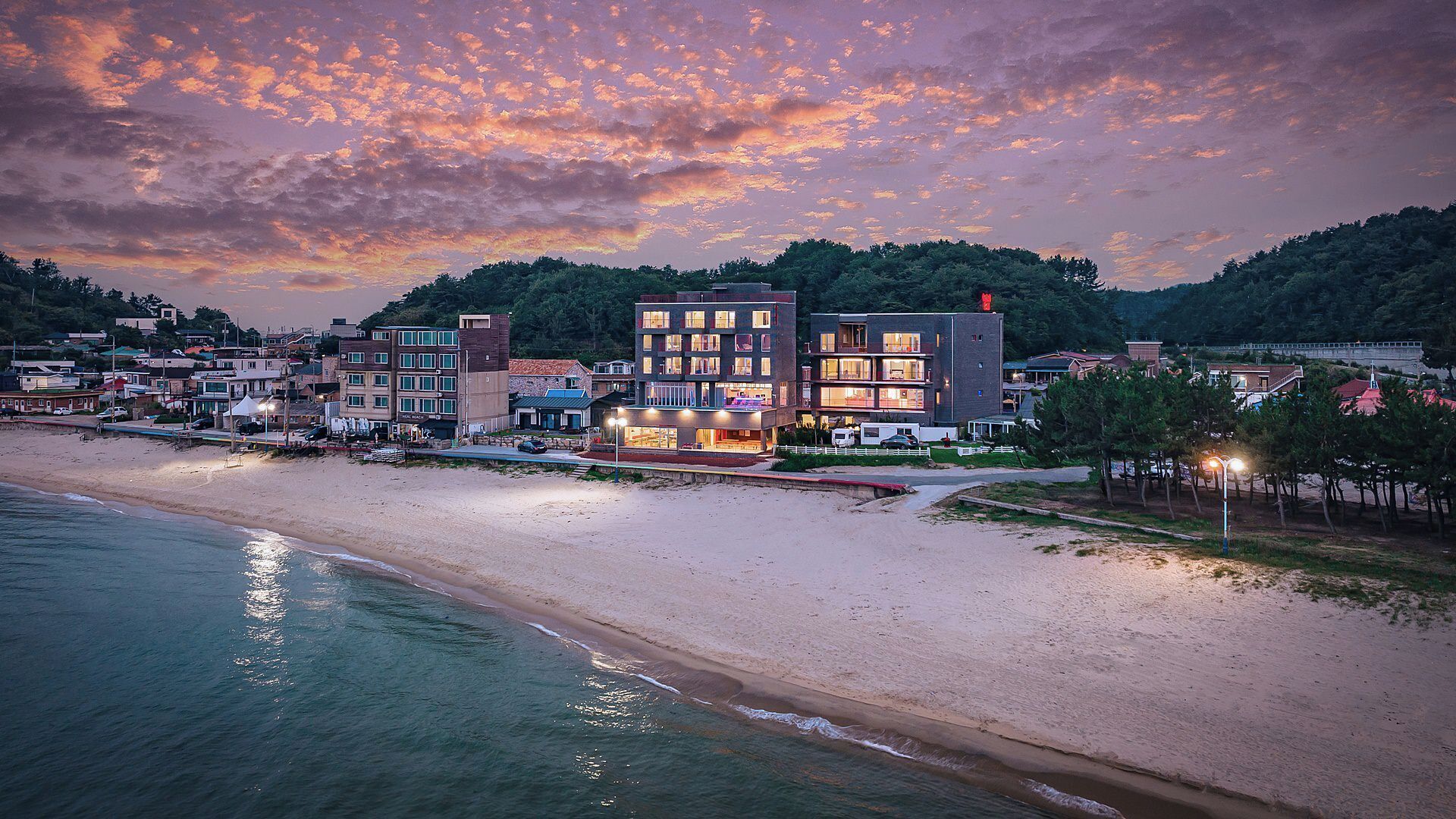 A coastal town with a beach, buildings, and a sunset sky.