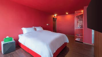 A hotel room with a large bed, a red wall, and a red storage unit.