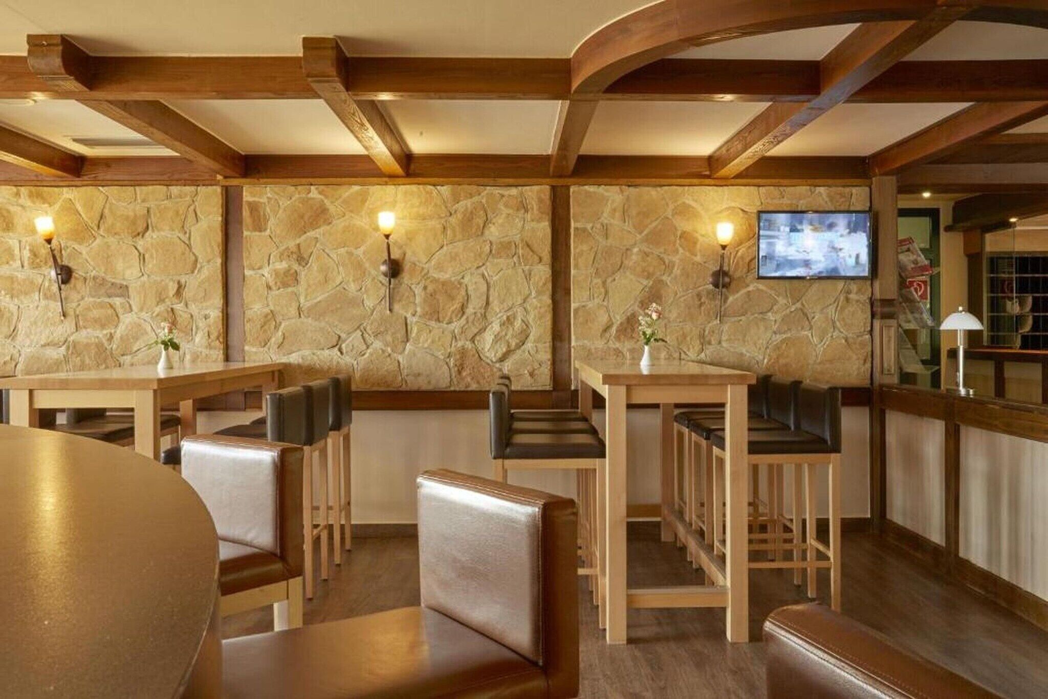 A restaurant with stone walls, wooden beams, and a TV mounted on the wall.