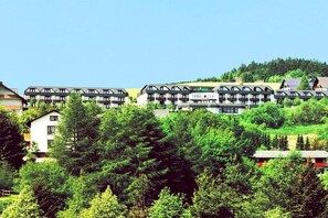 A multi-story hotel with balconies, surrounded by dense greenery and a clear sky.