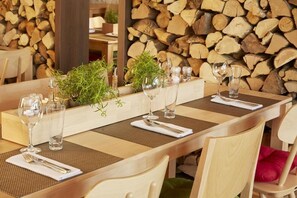 Una mesa de comedor dispuesta con cristalería, un centro de mesa con planta y un fondo de leña apilada.