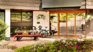 Entrada de un edificio con un banco, bicicletas y una cesta de flores colgante.