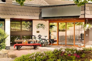 Ein Gebäudeeingang mit einer Bank, Fahrrädern und einem hängenden Blumentopf.