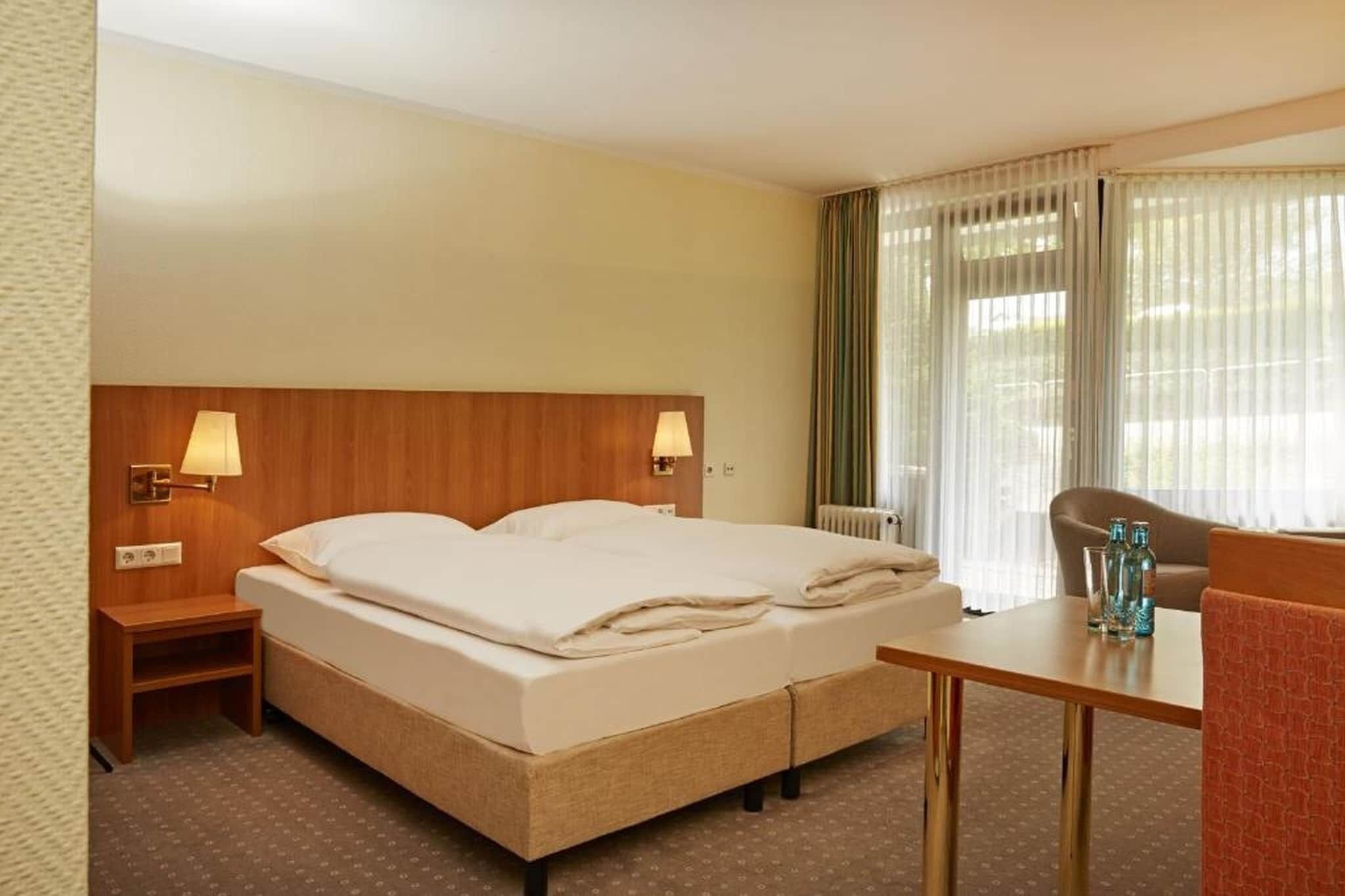 A hotel room with a bed, bedside lamps, a table, and a chair.