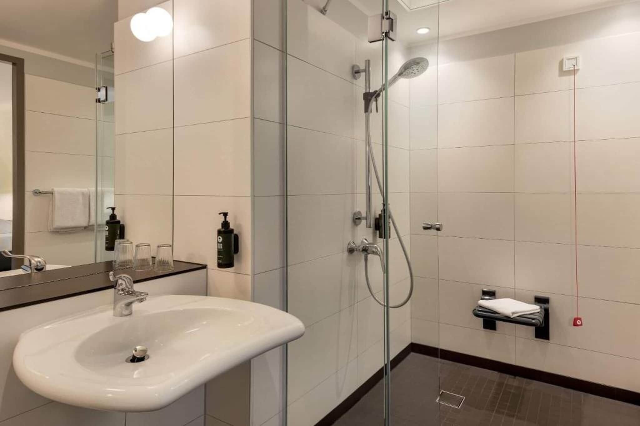 Een moderne badkamer met een glazen douchecabine, een witte wastafel en een spiegel.