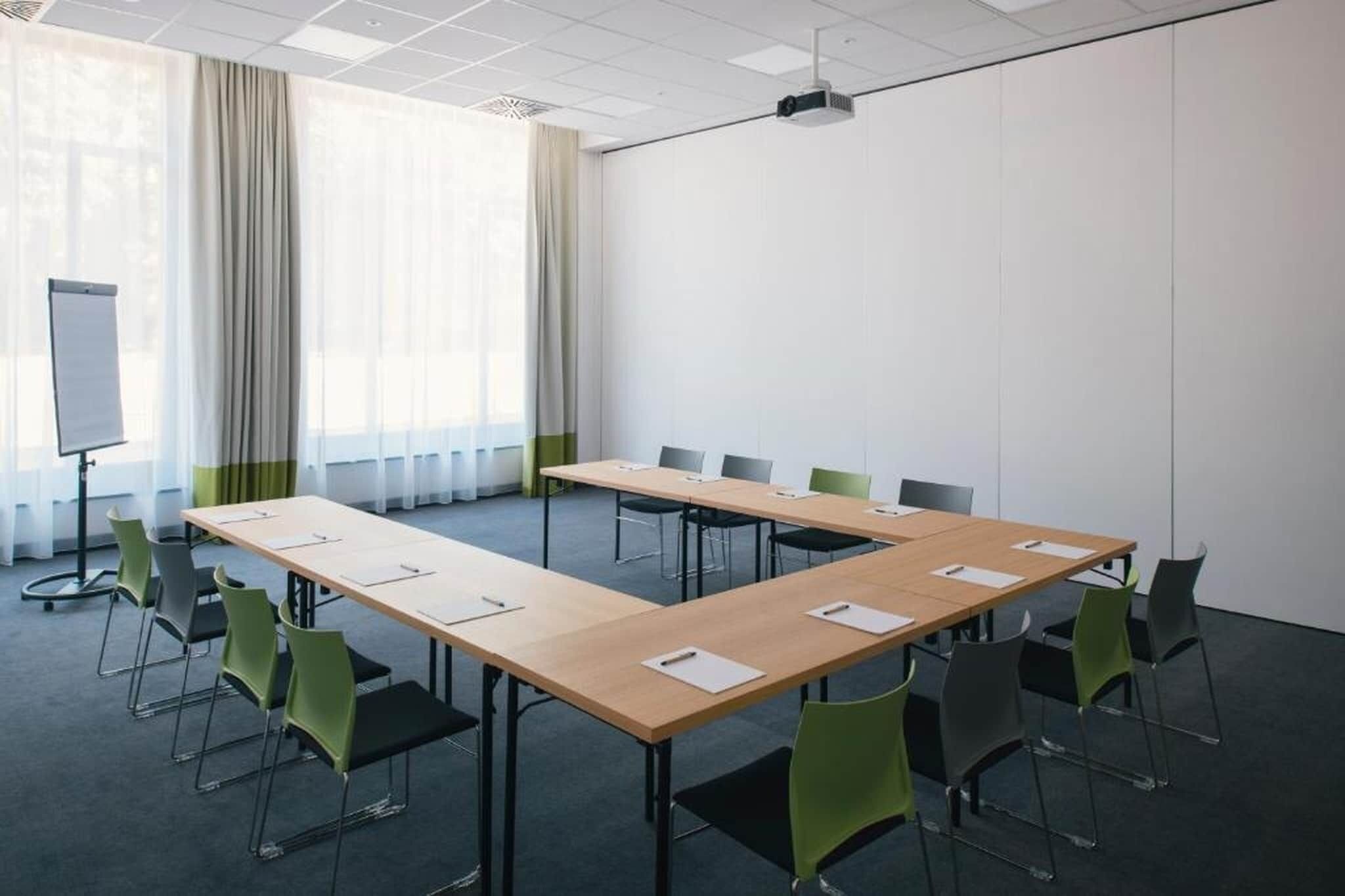 A conference room with a long table, green chairs, a whiteboard, and a projector.