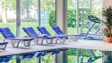A sunlit room with large windows, a treadmill, and striped lounge chairs.