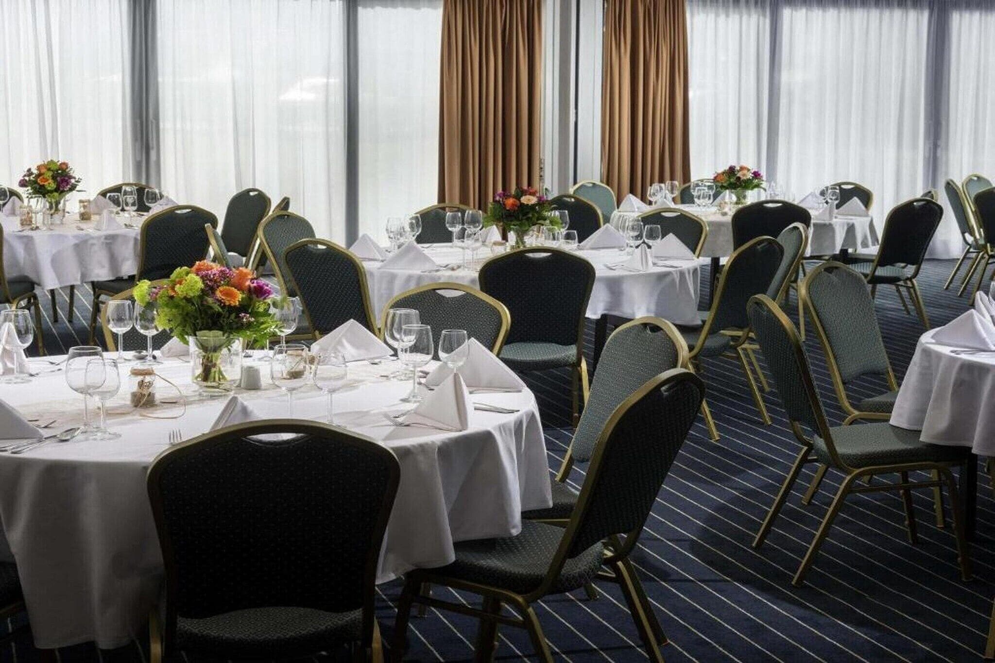 Un comedor de hotel con mesas redondas, sillas y centros de mesa florales.