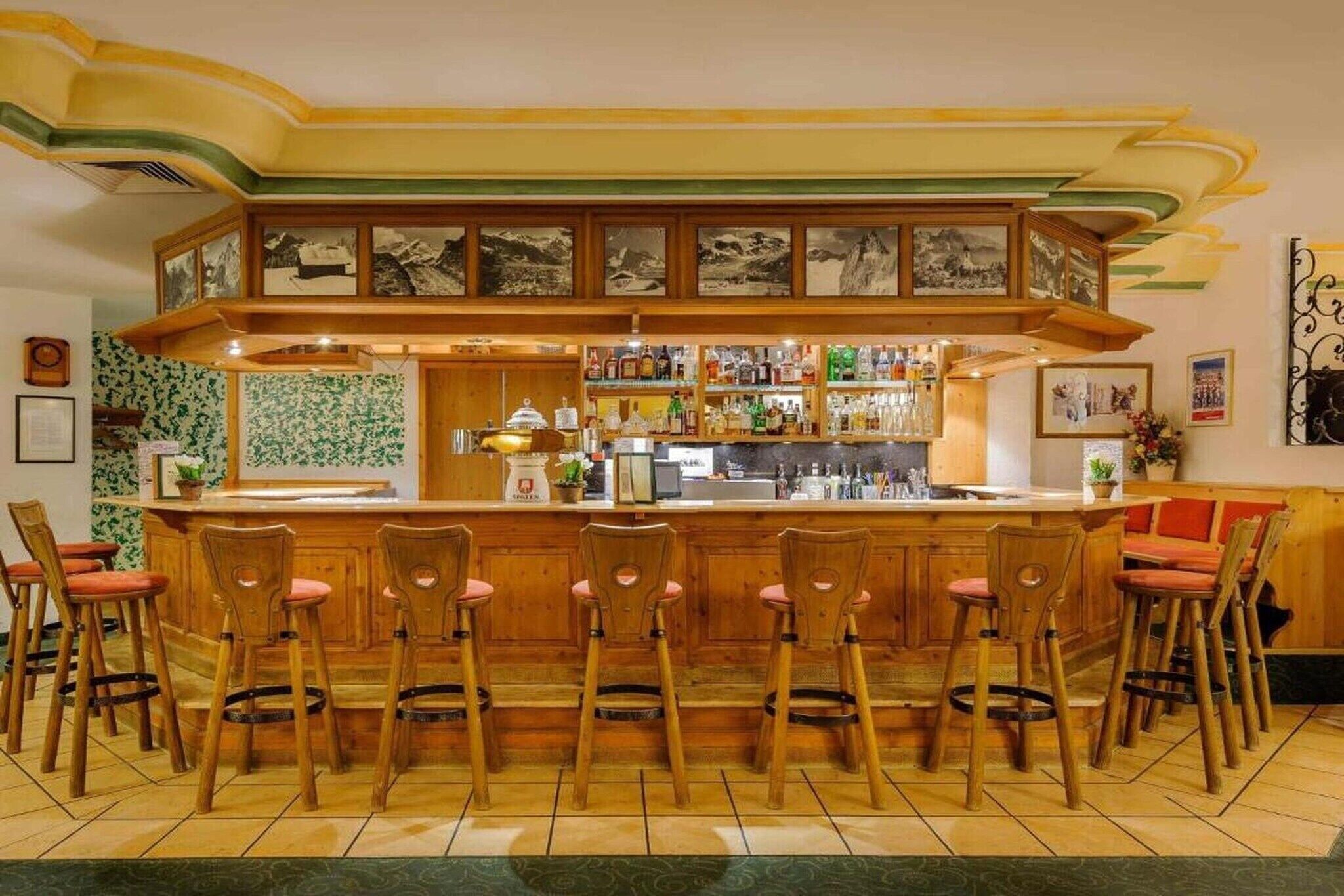A bar area with wooden bar stools, a counter with various bottles, and framed pictures on the wall.