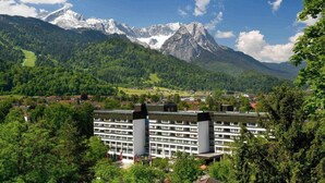 A hotel with a modern design, surrounded by lush greenery and mountains.