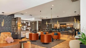 Um hall de hotel moderno com áreas de estar, um bar e uma mesa de recepção.