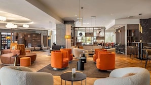 Um lobby de hotel moderno, com assentos laranja, parede de destaque em pedra e área de bar.