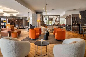 Eine moderne Hotelhalle mit orangefarbenen Sitzgelegenheiten, einer Wand aus Stein und einer Bar.