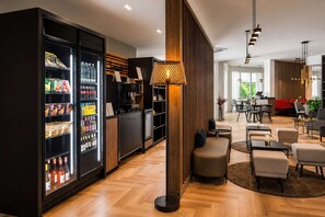 Eine moderne Hotelhalle mit einer Getränkeauswahl im Kühlschrank, einer Wand mit Holzvertäfelung und einer Sitzecke mit Tischen und Stühlen.