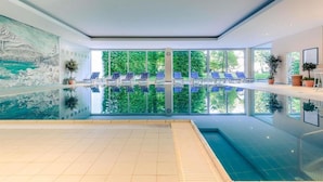 An indoor swimming pool with a view of trees through large windows, blue lounge chairs, and a mural on the wall. - Sunday Hotel Garmisch Partenkirchen Standard Twin Room (Garmisch-Partenkirchen)