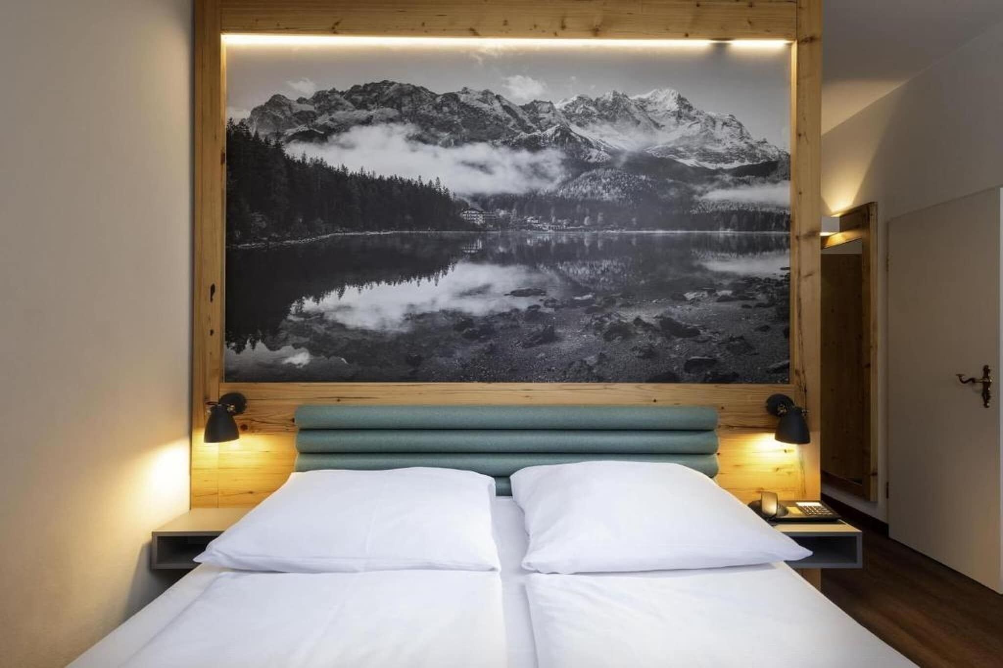 Un dormitorio con una cama, dos lámparas de noche y una gran fotografía enmarco de un paisaje montañoso.